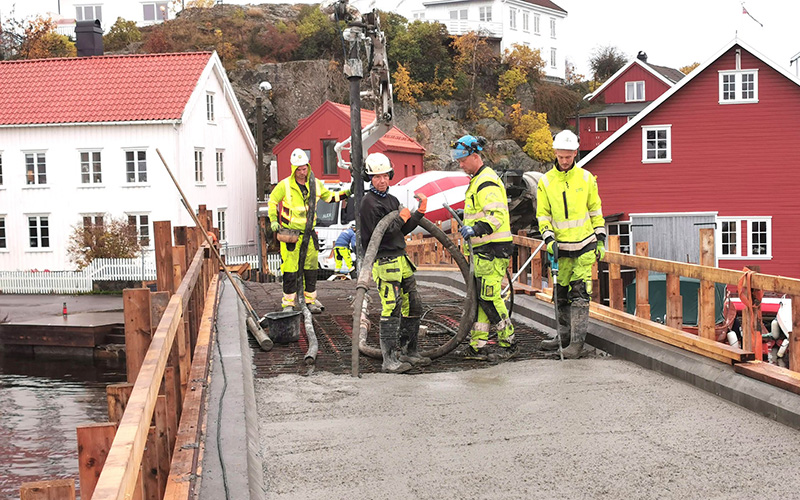 Arbeidere i arbeidsklær som jobber med forskaling, jernbinding og betongstøp av brokonstruksjoner